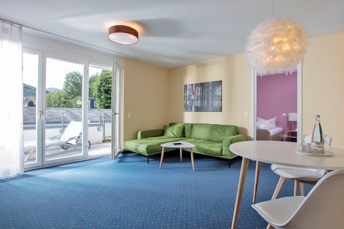 A room with yellow wall paint, a round table and a green couch in the Hotel Schwarzwald Panorama
