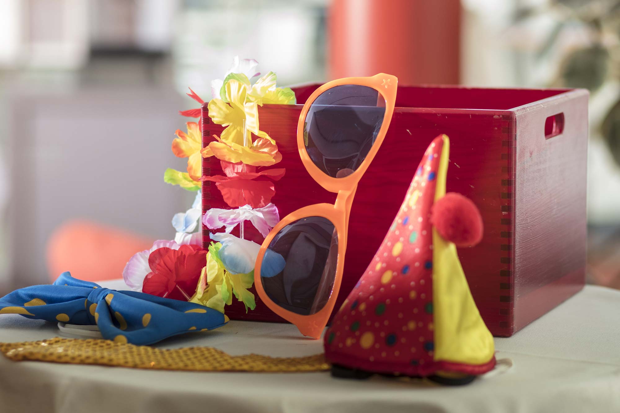 Holzkiste mit Utensilien für eine Feier: Partyhut, Krawatte, Schleife, Blumenkette und Sonnenbrille