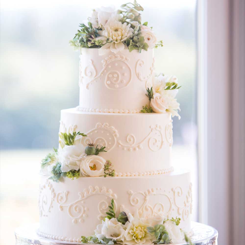 Dreistöckige weiße Hochzeitstorte mit Dekor und dezenter Blumendekoration