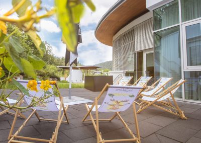 Auf einer Steinterrasse stehen Liegestühle vor grüner Kulisse im Hotel Schwarzwald Panorama