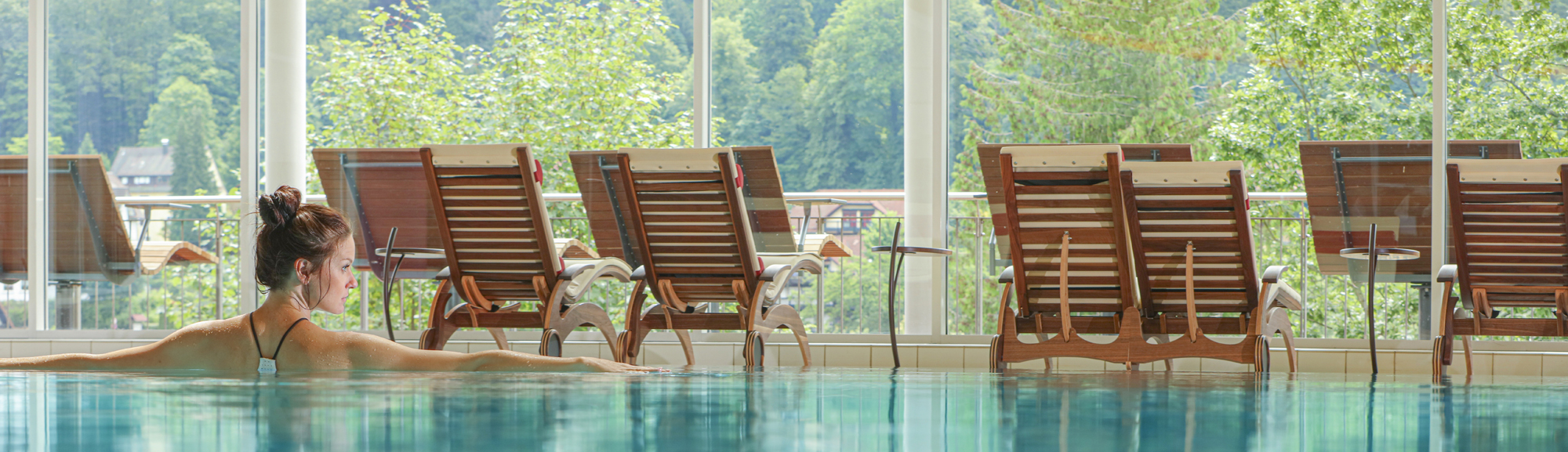 Eine Frau nimmt ein Bad im SPA, Wellness, Pool Bereich, vor Liegestühlen und grüner Kulisse im Hotel Schwarzwald Panorama.