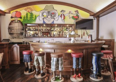 Vor einer Wand mit Cartoon Bemalung steht eine dunkelbraune Bar, mit Beinen als Barhocker.Die Schwarzwald Bar im Hotel Schwarzwald Panorama