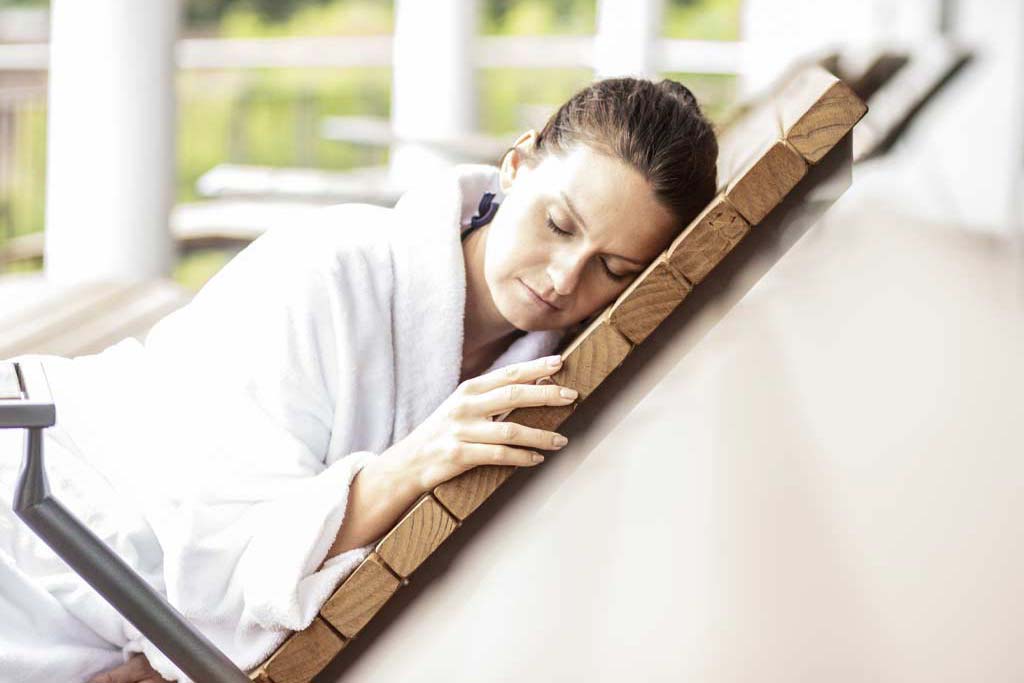 Eine Frau in weißem Bademantel schläft tiefenentspannt im Wellnessbereich des Selfness Hotel SCHWARZWALD PANORAMA