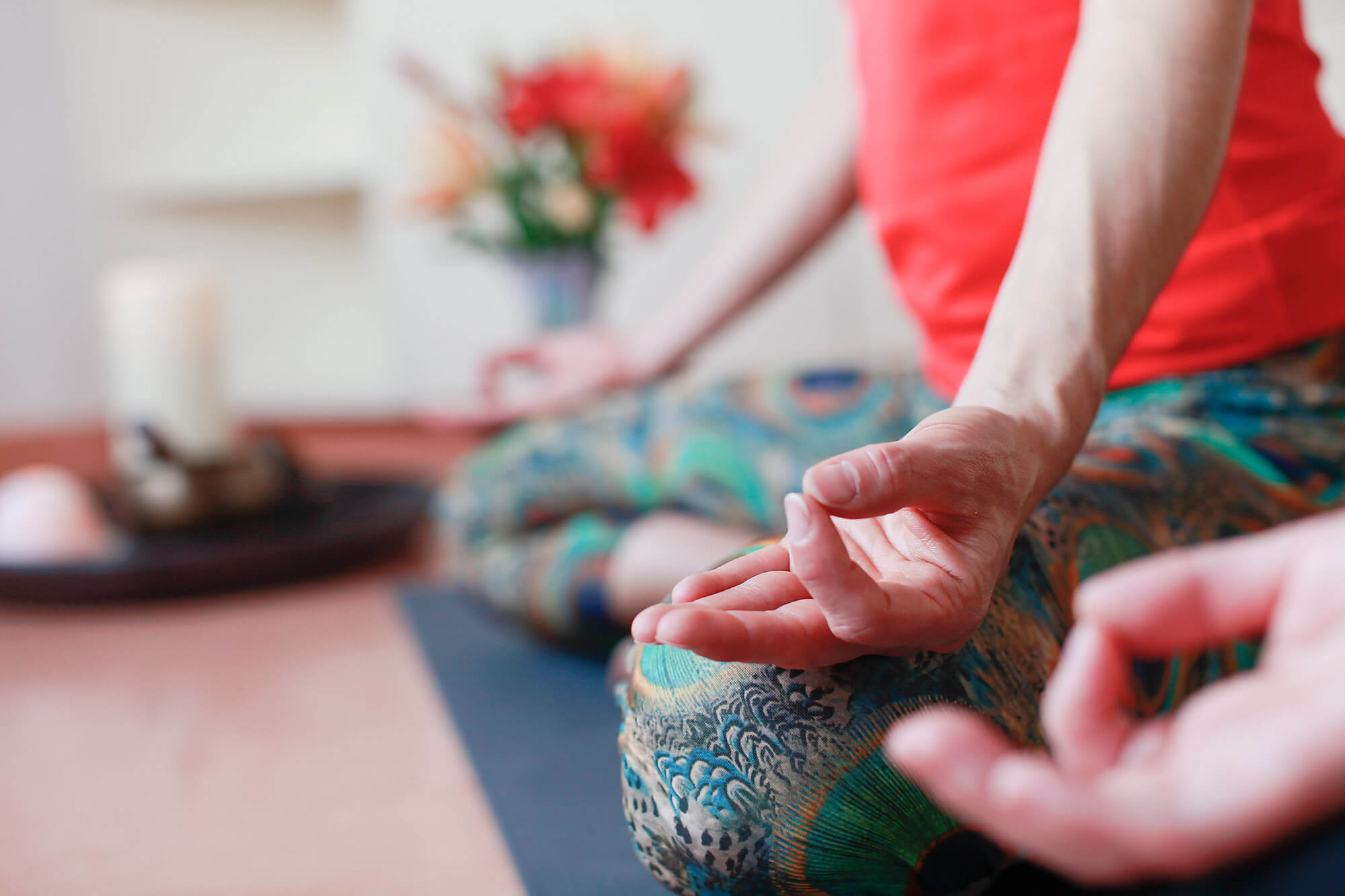 Eine Person sitzt auf dem Boden, die Hände formen eine Meditationsgeste.